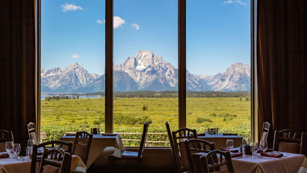 Scenic restaurant interior with large windows overlooking Grand Teton mountains, highlighting dining at hotels near U.S. National Parks.