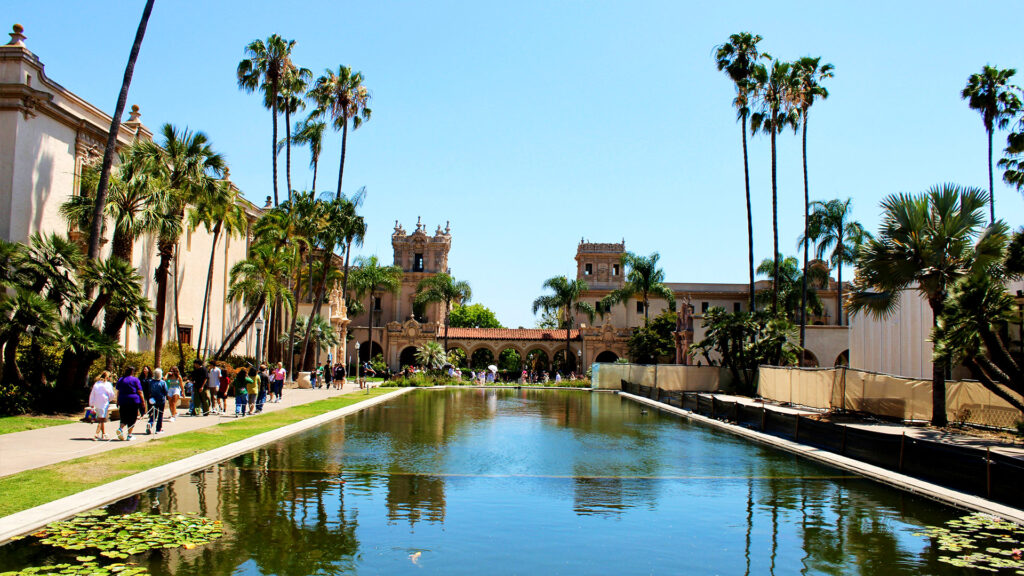 Visitors walking along the reflecting pool at Balboa Park surrounded by palm trees on a sunny San Diego family vacation