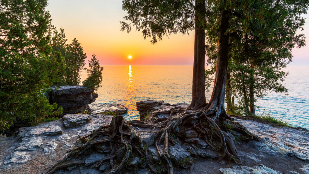 A stunning view of the sun setting over the ocean with a rocky shoreline, an ideal place for a quiet summer retreat.