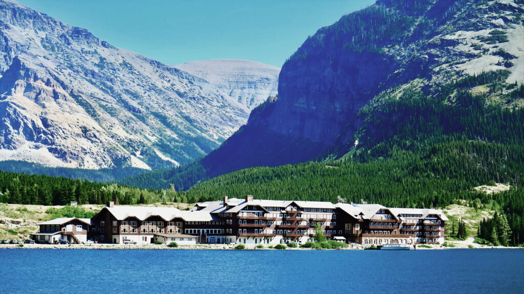 Large lakeside lodge surrounded by towering mountains and forest, representing classic hotels near U.S. National Parks.