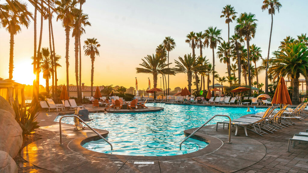 Palm-lined resort pool glowing at sunset with lounge chairs and guests relaxing during a San Diego family vacation
