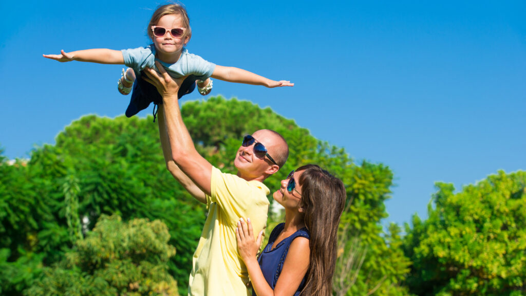 Parents lifting a child in the air while playing in a sunny park, enjoying quality time on a San Diego family vacation