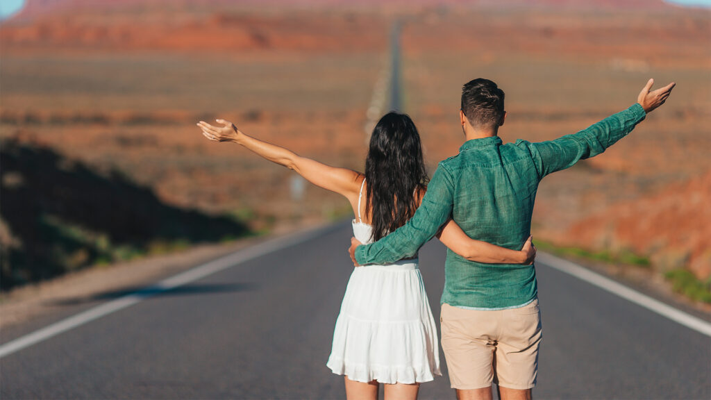 A couple standing on an empty road with their arms outstretched, capturing a scenic view of a Utah landscape.