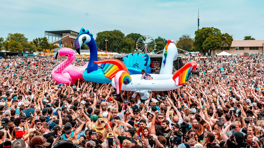 Festival crowd with large inflatable flamingos and swans at a vibrant summer music festival.