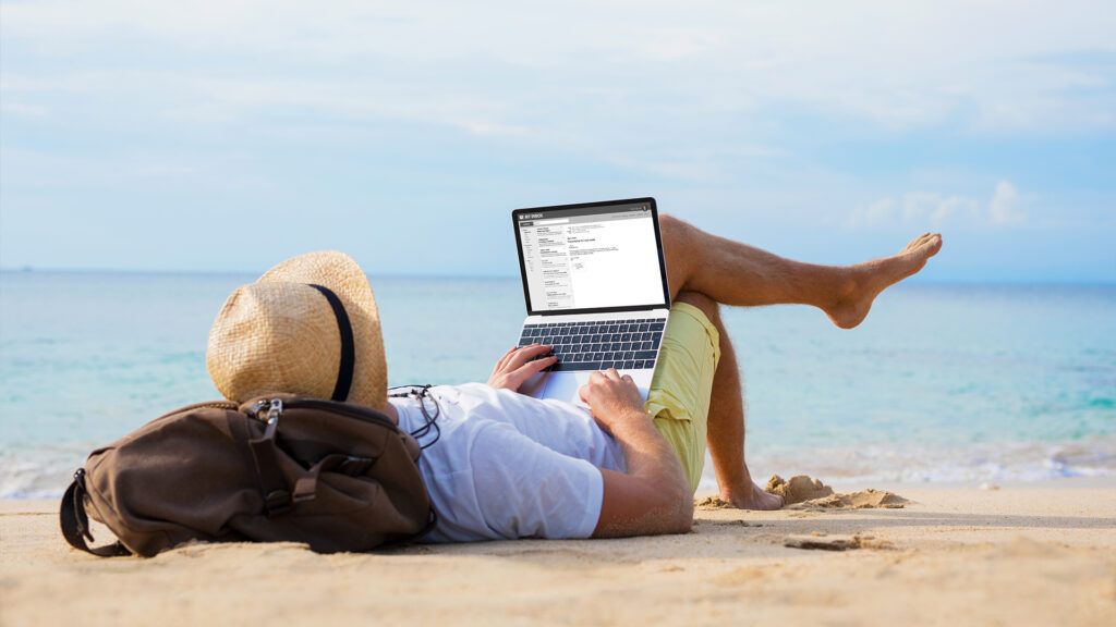 Man working on his laptop while lying on the beach, showcasing the rise of short trips for work and leisure balance.