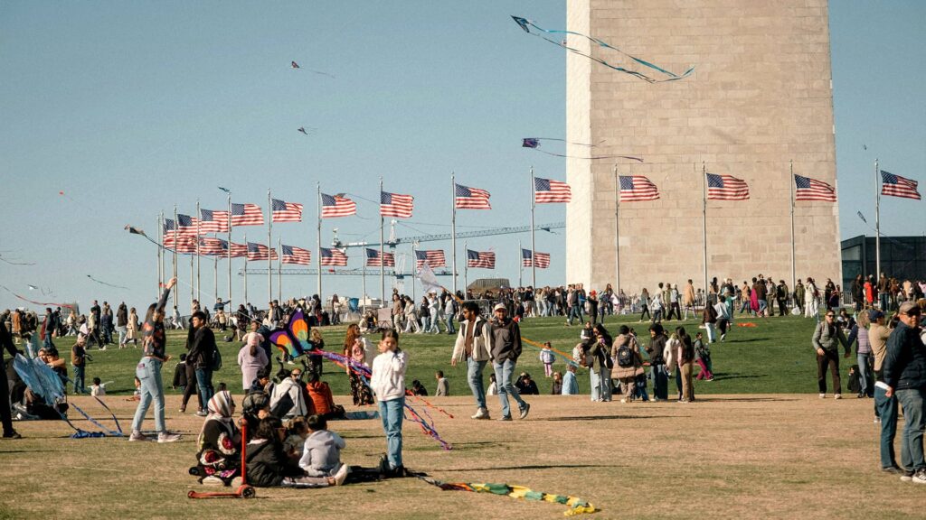 A family enjoying the outdoors with flags flying high near the Washington Monument, and people flying kites.