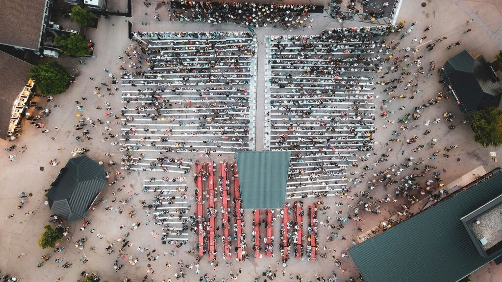 Aerial view of a large summer festival crowd arranged in the shape of an American flag, with benches and tents.