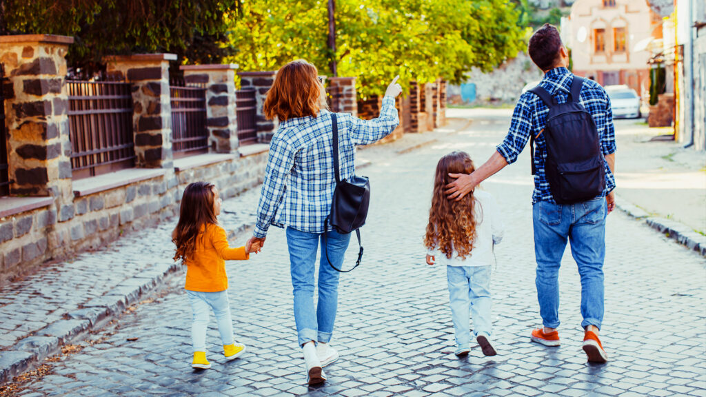A family walking hand in hand on a city street, looking excited as they explore urban sights on their summer vacation.