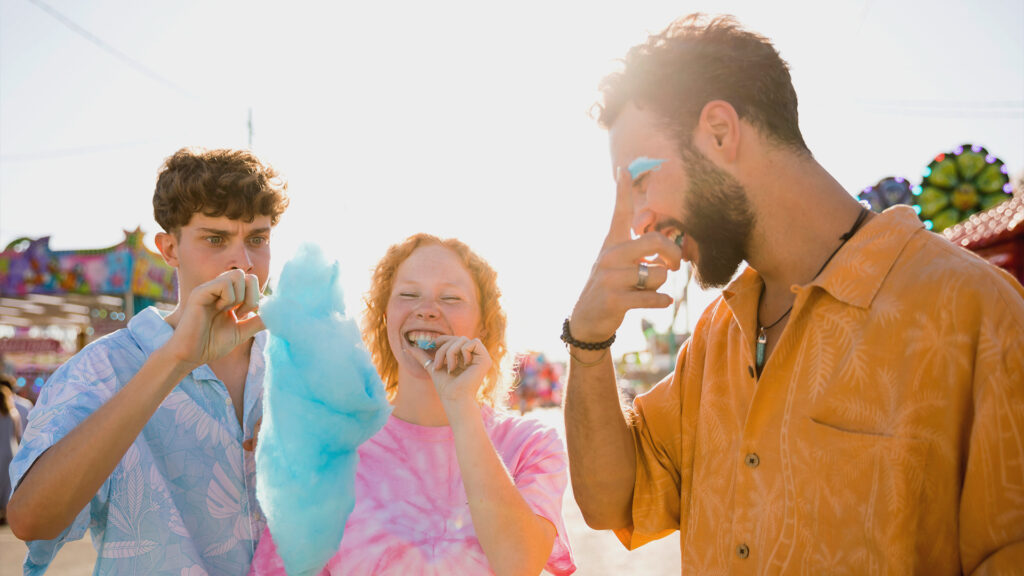 Group of friends enjoying cotton candy at a summer fair, smiling in the sunlight.