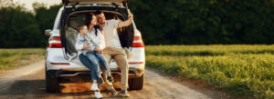 A family of three taking a selfie while sitting on the back of their car parked on a scenic road, enjoying a road trip.