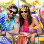 Group of friends smiling and posing at a vibrant summer festival, wearing colorful clothes and accessories.