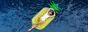 Woman relaxing on a pineapple-shaped float in the pool, embodying the popular summer travel trends of relaxation and fun.
