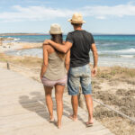 Couple walking down a boardwalk by the beach, enjoying a short romantic trip to a coastal destination.
