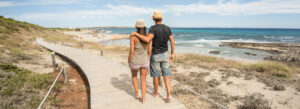 Couple walking down a boardwalk by the beach, enjoying a short romantic trip to a coastal destination.